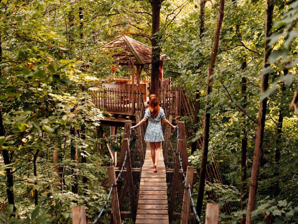 Jeune femme traversant un pont suspendu entre 2 cabanes dans les arbres
